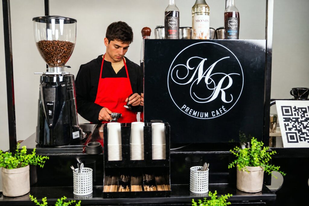 Barista von Maitre Royal an der Kaffeemühle des Kaffeerads, vor ihm Becher für die nächsten Bestellungen