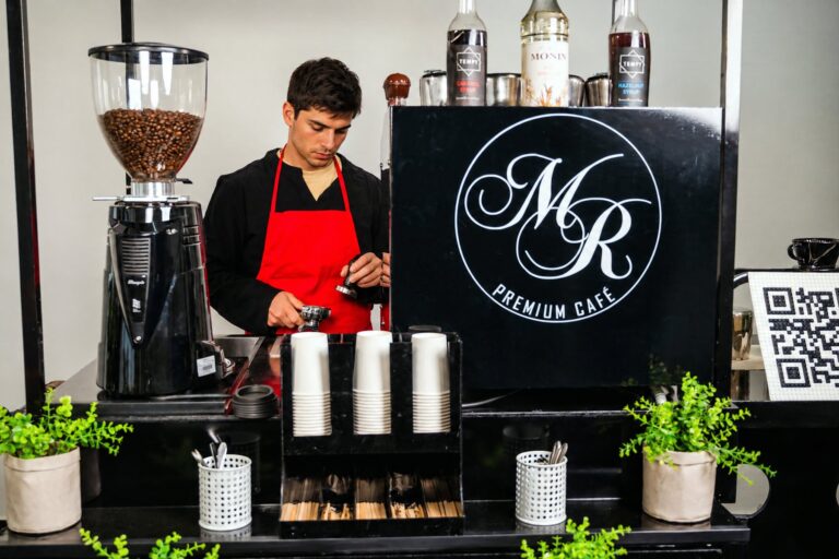 Barista von Maitre Royal an der Kaffeemühle des Kaffeerads, vor ihm Becher für die nächsten Bestellungen
